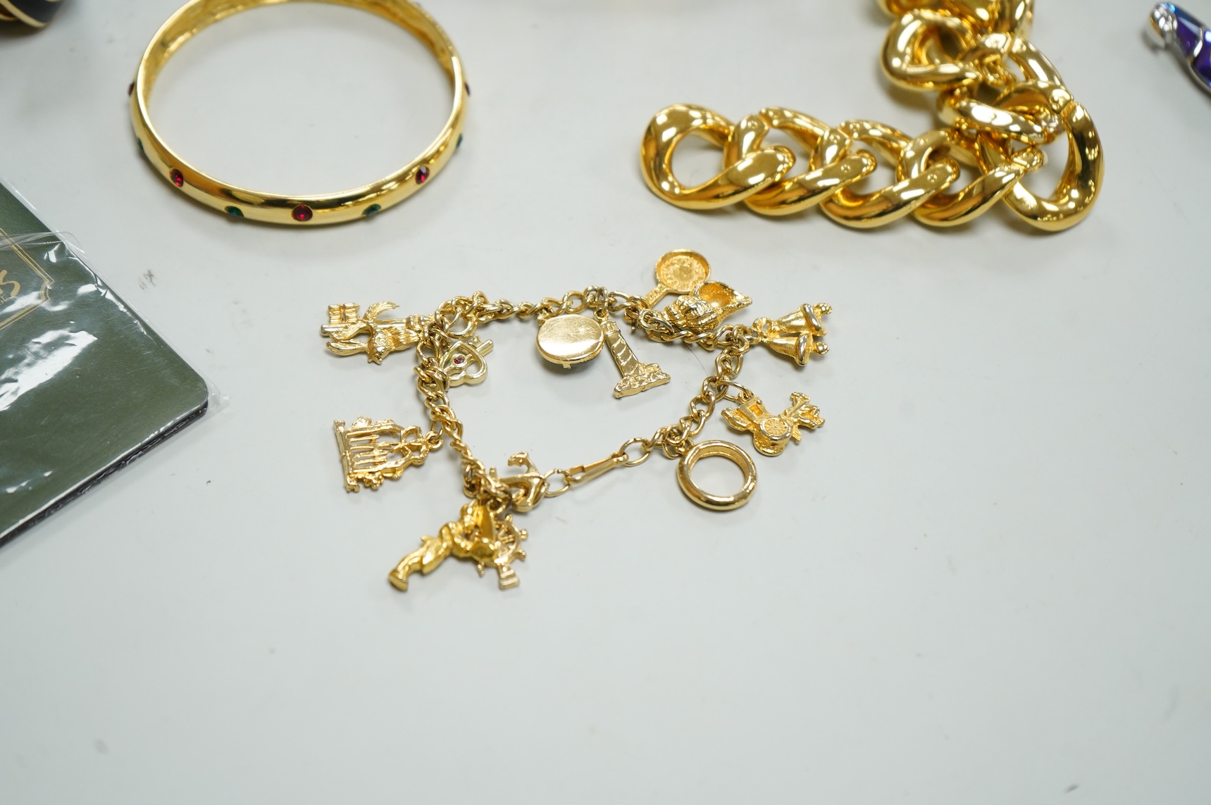 A small group of assorted costume jewellery including a 925 and paste set brooch and pair of ear clips and a gilt metal charm bracelet.